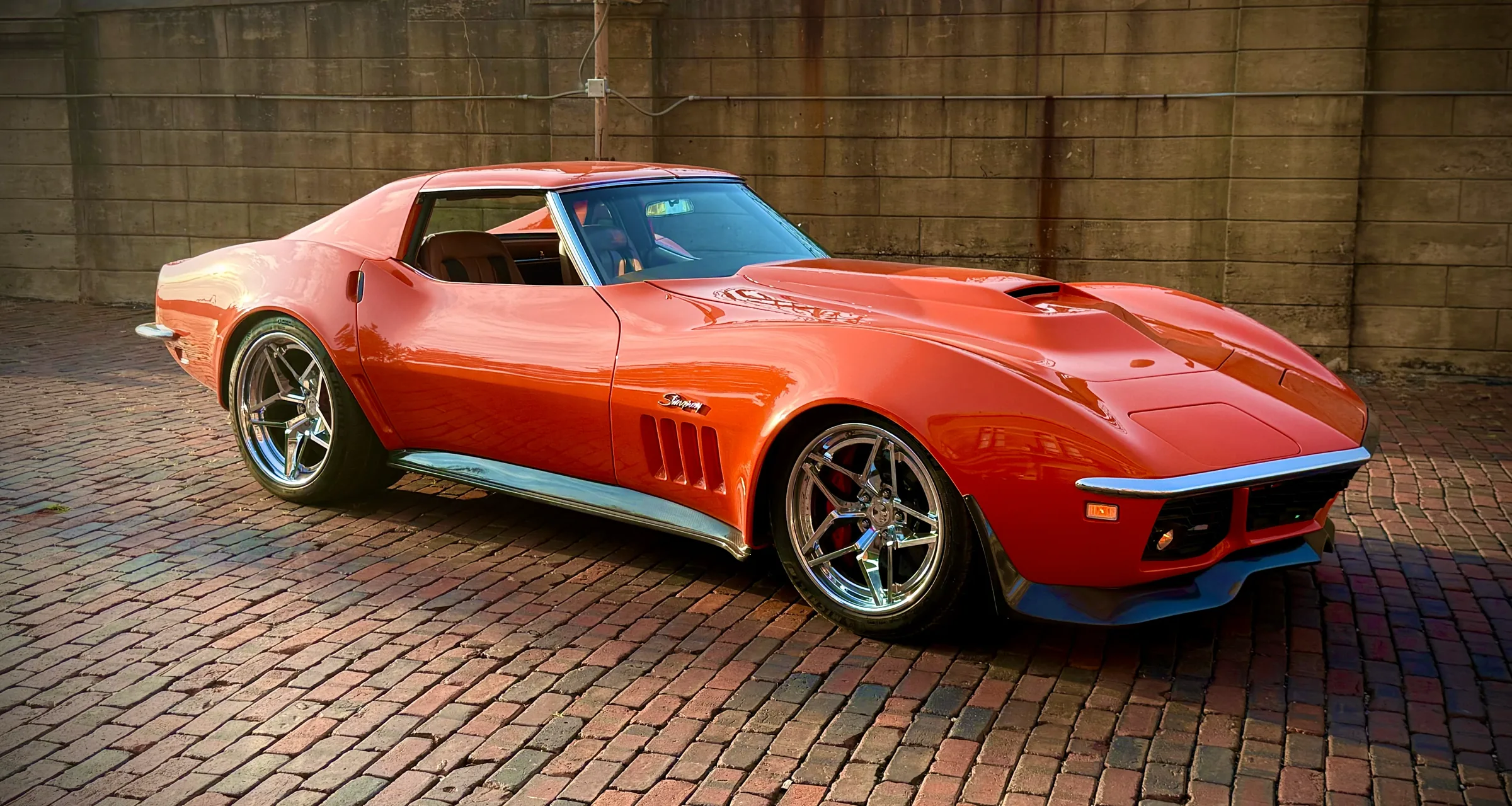 Orange classic Corvette in a street setting, front three-quarter view.